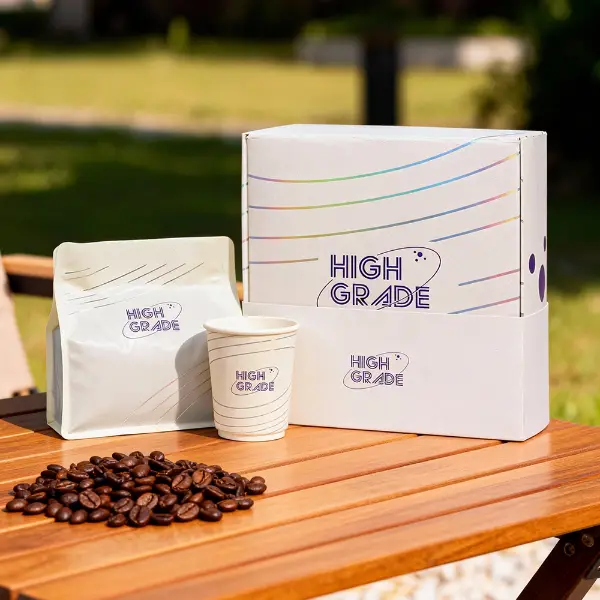 カスタムブランドのコーヒーボックスと、それに合うコーヒーバッグと紙コップが木製のテーブルの上に展示されています
